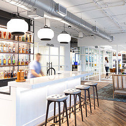 A bar with stools and a couple people in the background.